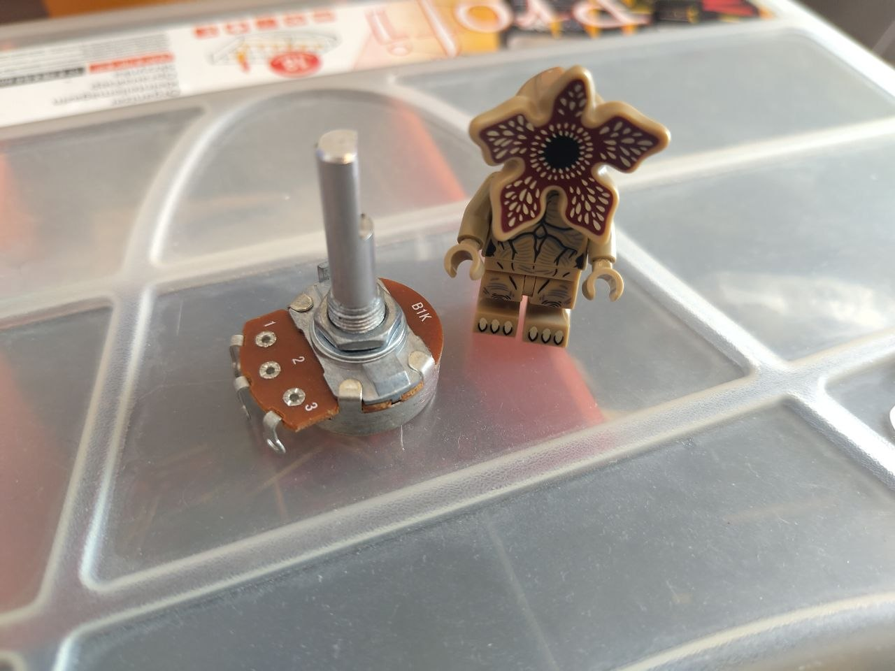 Large bare potentiometer beside a monster minifigure on an electronics storage box, showing their comparable size